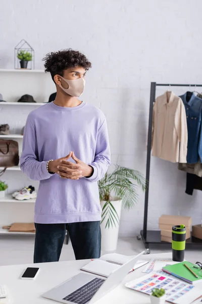 Propriétaire afro-américain de showroom avec masque de protection debout près des appareils et ordinateur portable sur la table — Photo de stock