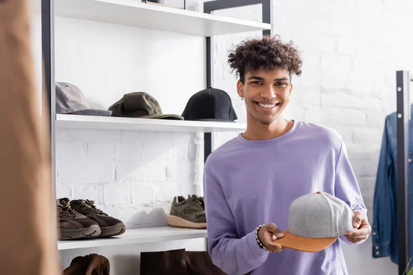Lächelnder afrikanisch-amerikanischer Showroom-Besitzer blickt in die Kamera, während er eine Mütze hält — Stockfoto