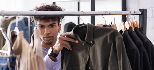 Young african american owner of showroom working with clothes on hangers on blurred foreground, banner — Stock Photo
