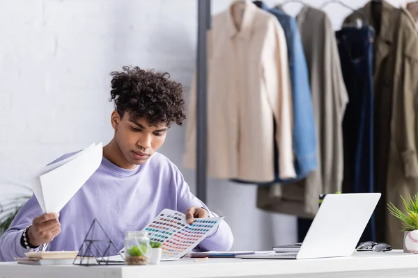 Afro americano propietario de sala de exposición celebración de muestras de colores cerca de la computadora portátil - foto de stock
