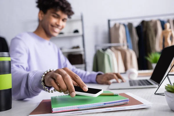 Smartphone en main du propriétaire afro-américain du showroom en utilisant un ordinateur portable sur fond flou — Photo de stock