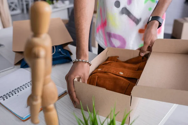 Cropped view of african american owner of showroom holding carton box with shirt near notebook — Stock Photo