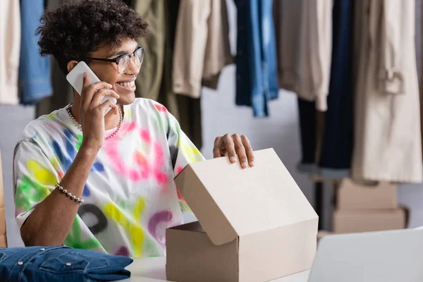 Afroamerikanischer Showroom-Besitzer spricht auf Smartphone in der Nähe von Kleidung und Karton — Stockfoto