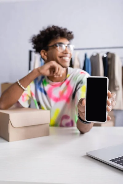 Cellphone with blank screen in hand of african american owner of showroom on blurred background — Stock Photo