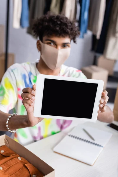 Tablet digital com tela em branco nas mãos do proprietário do showroom americano africano em máscara protetora perto do pacote na loja — Fotografia de Stock