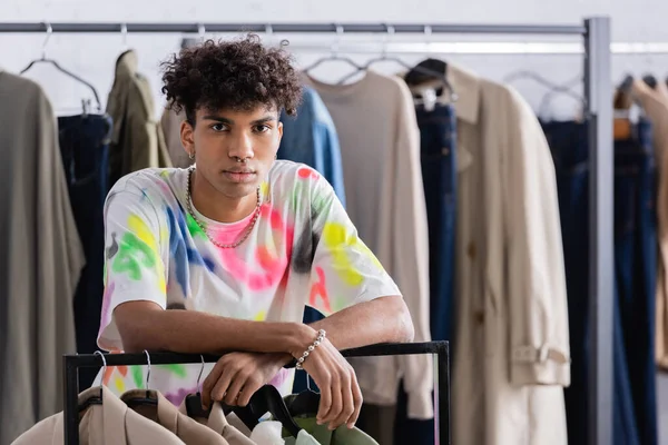 Joven hombre de negocios afroamericano de pie cerca de la ropa en el estante colgante en el showroom - foto de stock