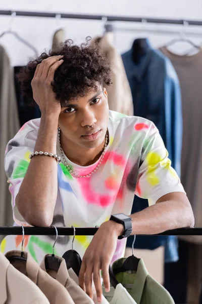 African american showroom owner looking at camera near clothes on hanging rack — Stock Photo