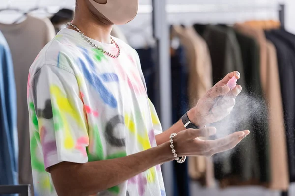 Cropped view of african american retailer in protective mask using hand sanitizer — Stock Photo