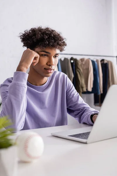 Propriétaire d'un showroom afro-américain regardant un ordinateur portable près d'une balle de baseball au premier plan flou — Photo de stock