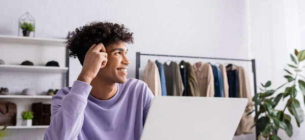 Smiling african american small business owner looking away near laptop in showroom, banner — Stock Photo