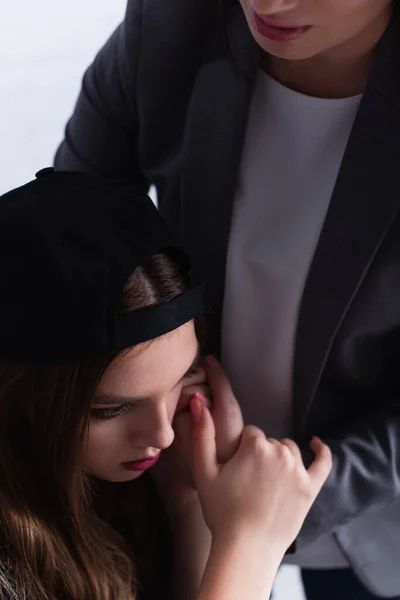 Sad teenage girl in cap hugging with psychologist on blurred background — Stock Photo