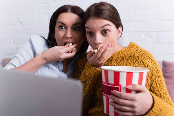 Adolescent attentif fille et mère regarder film sur ordinateur portable et manger du pop-corn dans la chambre — Photo de stock