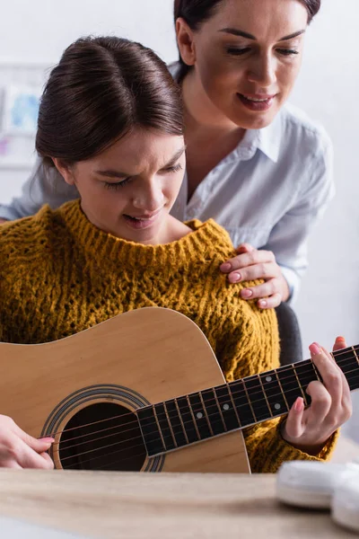 Teenagermädchen beißt Lippen, während sie lernt, wie man nahe der Mutter Akustikgitarre spielt — Stockfoto