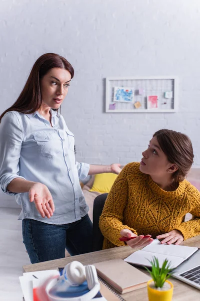 Mécontent mère regardant adolescente fille faire des devoirs près d'un ordinateur portable — Photo de stock