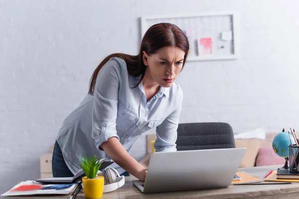 Mujer mirando a la computadora portátil mientras se escabulle por casa - foto de stock
