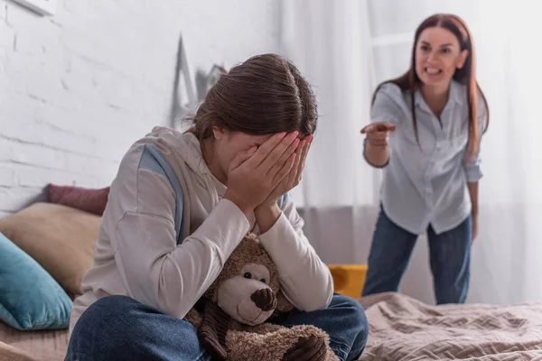 Adolescent fille couvrant visage près de mère en colère sur fond flou — Photo de stock