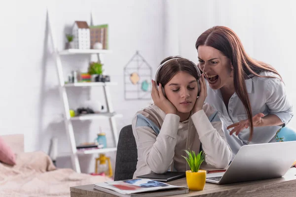 Mother screaming at teenage girl in wireless headphones sitting at desk — Stock Photo