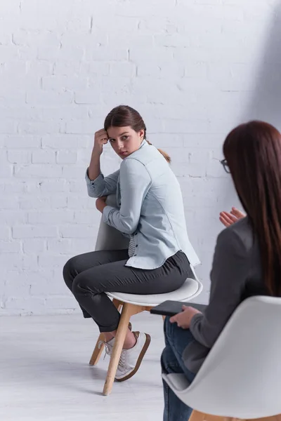 Upset teenage girl sitting and looking at psychologist on blurred foreground — Stock Photo