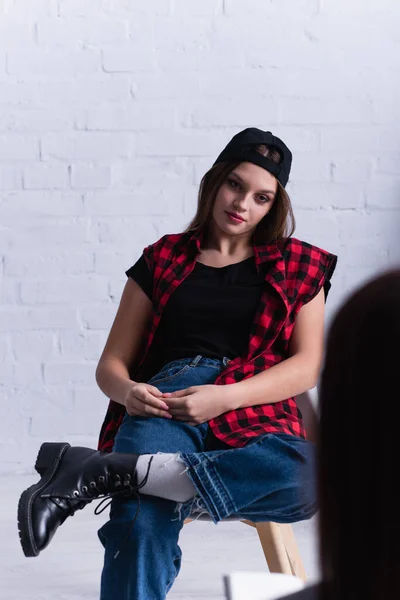 Sad teenage patient in cap sitting near psychologist on blurred foreground — Stock Photo