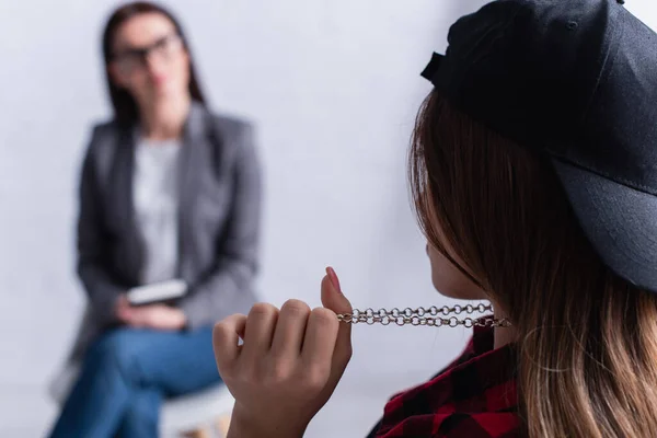 Teenage patient pulling chain on neck near psychologist on blurred background — Stock Photo