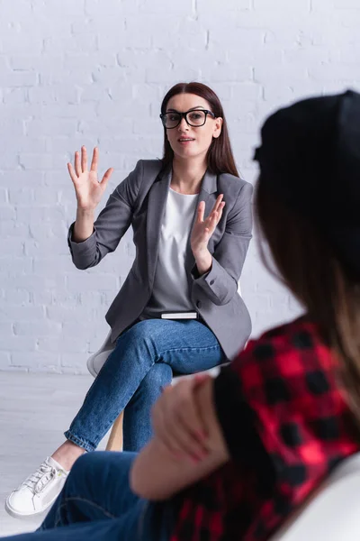 Psychologist in glasses gesturing while looking at teenager on blurred foreground — Stock Photo