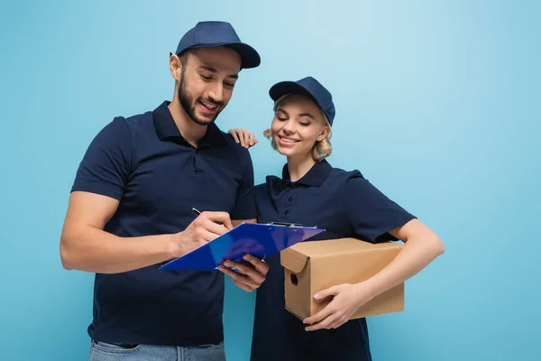 Árabe entrega homem escrevendo na área de transferência perto sorrindo colega com parcela isolada no azul — Fotografia de Stock