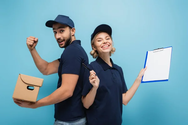 Mensajero sonriente apuntando con pluma a colega árabe mostrando el gesto de éxito en azul - foto de stock