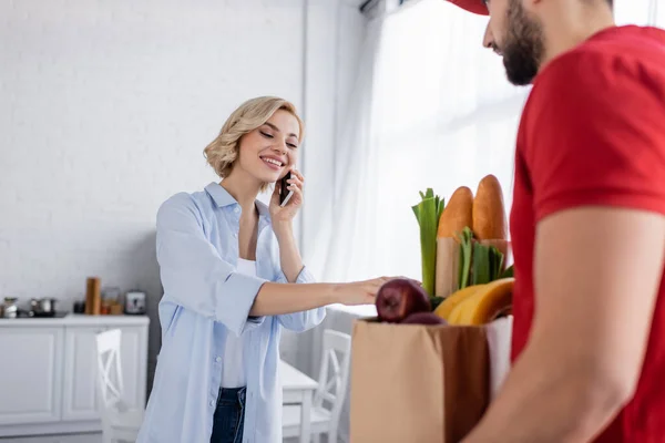 Pretty woman calling on mobile phone near arabian delivery man on blurred foreground — Stock Photo