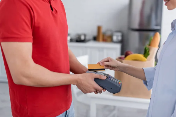 Cropped view of woman holding credit card near delivery man with payment terminal — Stock Photo