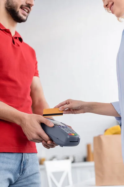 Частковий вид усміхненого доставки чоловік тримає термінал оплати поруч з жінкою з кредитною карткою — стокове фото