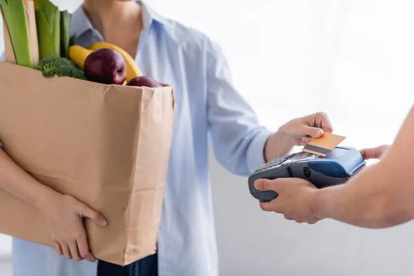 Vista recortada de entrega hombre celebración terminal de pago cerca de la mujer con tarjeta de crédito sobre fondo borroso — Stock Photo