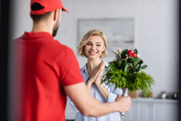 Pleased woman near arabian delivery man holding bouquet on blurred foreground — Stock Photo