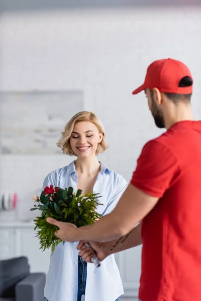 Young arabian courier holding bouquet near pretty woman, blurred foreground — Stock Photo