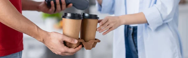 Vista recortada del repartidor hombre sosteniendo café para acercarse a la mujer sobre fondo borroso, pancarta - foto de stock