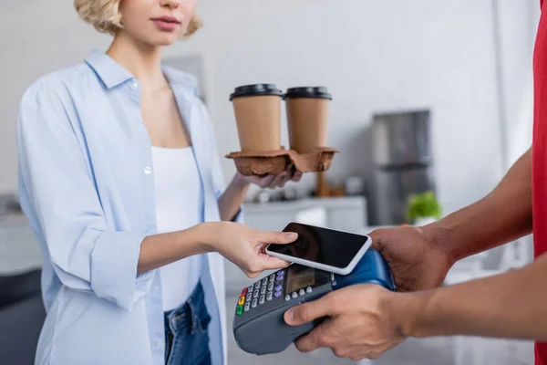 Partial view of delivery man holding payment terminal near woman with mobile phone — Stock Photo