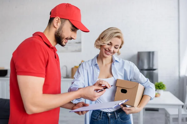 Homme de livraison musulman donnant stylo et presse-papiers à la femme souriante tenant colis — Photo de stock