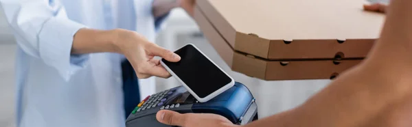 Vista parziale del fattorino che tiene scatole di pizza e terminale di pagamento vicino alla donna con smartphone, banner — Foto stock