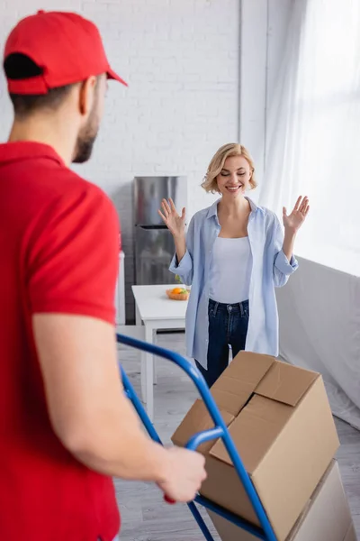 Excited woman showing wow gesture near delivery man with boxes on blurred foreground — Stock Photo