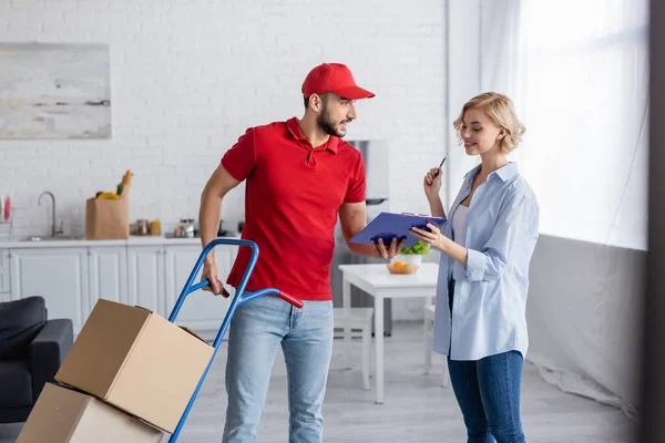 Arabian delivery man giving clipboard to blonde woman on blurred foreground — Stock Photo