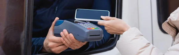 Visão cortada do homem de entrega segurando terminal de pagamento perto da mulher com telefone móvel, banner — Fotografia de Stock