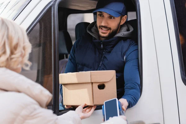 Arabian postman holding box and payment terminal near woman with mobile phone on blurred foreground — Stock Photo