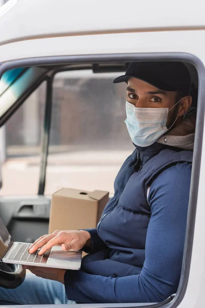 Homme de livraison musulman en masque médical tapant sur ordinateur portable en voiture — Photo de stock