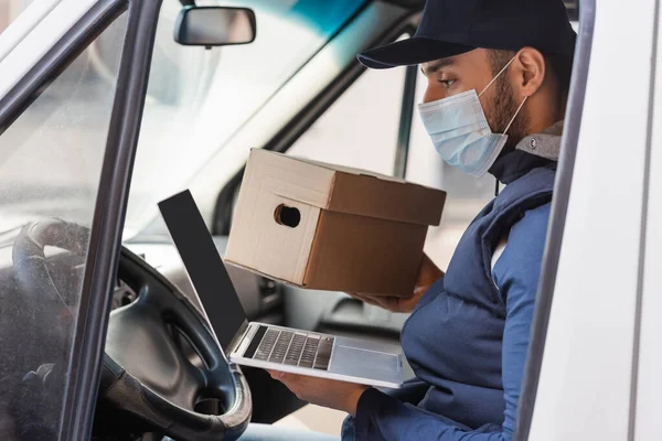 Muslim courier in medical mask sitting with laptop in car — Stock Photo