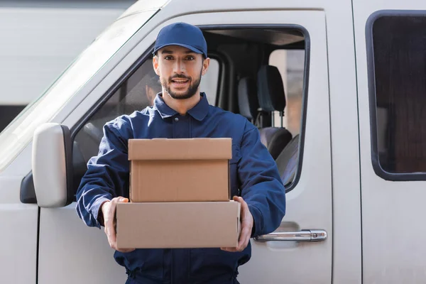 Young arabian postman holding parcels and looking at camera near car — Stock Photo