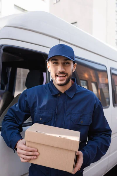 Joyeux facteur arabe regardant caméra tout en tenant colis — Photo de stock