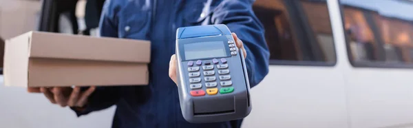 Cropped view of delivery man with carton box and payment terminal on blurred background, banner — Stock Photo