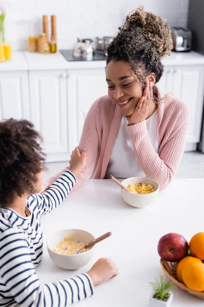 Africano americano niño tocando mano de feliz madre durante el desayuno, borrosa primer plano - foto de stock
