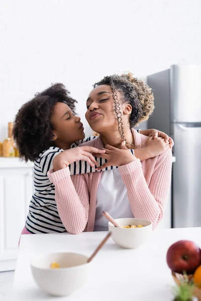 African american girl embracing and kissing mother in kitchen, blurred foreground — Stock Photo