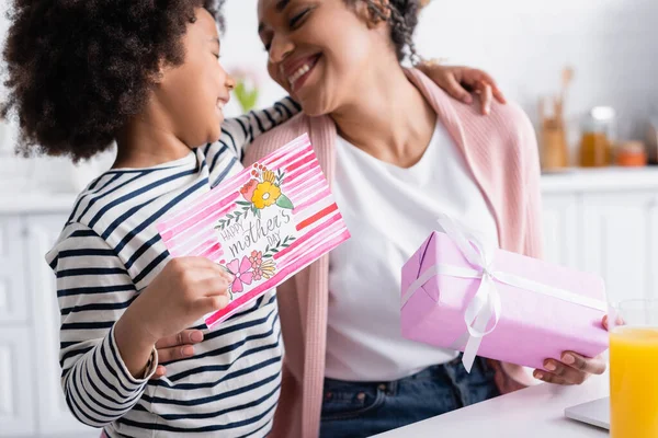 Happy african american girl holding happy mothers day card near pleased mom on blurred background — Stock Photo