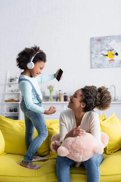 Alegre africano americano niño en auriculares mostrando ganar gesto cerca alegre madre - foto de stock